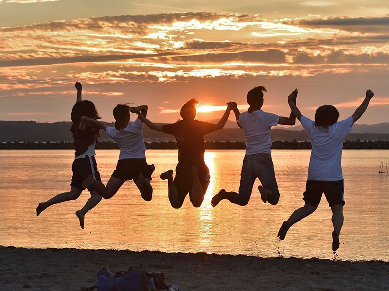 夕暮れの野辺地海浜公園：夕日に向かってジャンプをする学生たち